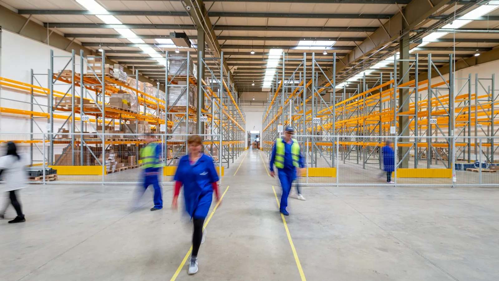 Trabajadores recorriendo el pasillo central de un almacén entre estanterías